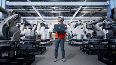trabajador de una fábrica con una computadora portátil revisando robots en una instalación de fabricación moderna