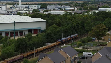 Aerial-view-tracking-a-freight-train-with-a-rising-reveal-of-the-town-of-Royston-in-England,-UK