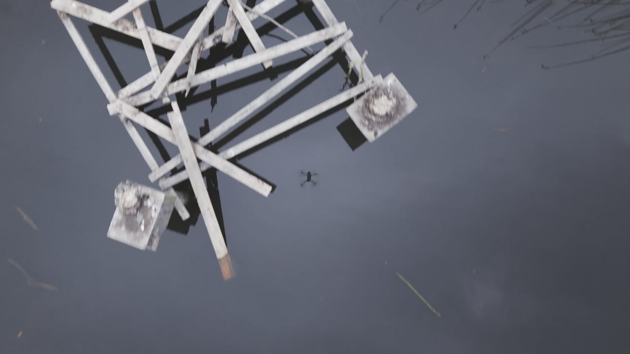 Drone video capturing serene reflections of wooden structures on still water surface at pond in Kilsyth South park, Australia. Calm ambiance with muted colors and delicate reflections.