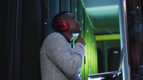 African-american-male-computer-technician-using-laptop-working-in-business-server-room