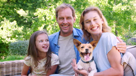 white parents and daughter sit with their dog in the garden