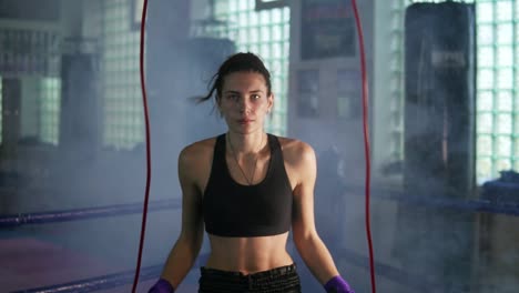 Young-female-boxer-with-her-hands-wrapped-in-bandage-jumping-on-the-skipping-rope-in-a-gym-with-smoke.-Slow-Motion-shot