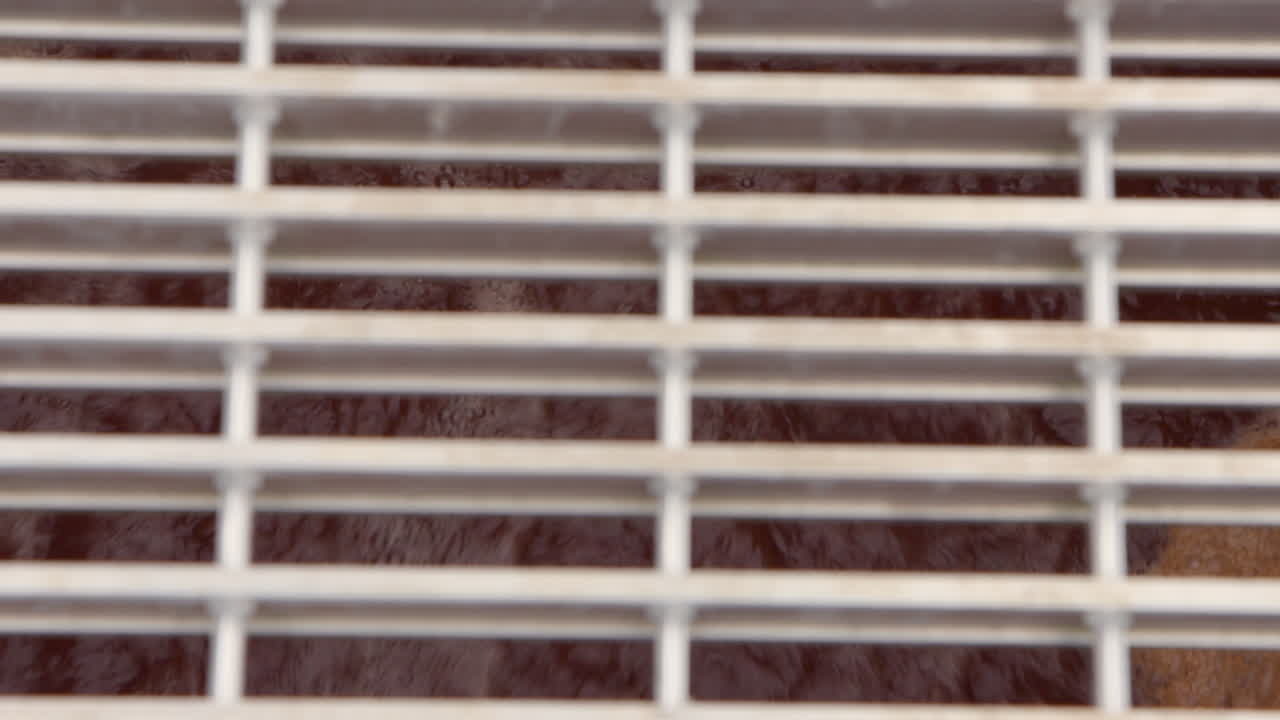 Sewage water churns and bubbles below a metal grate crosswalk in a wastewater treatment plant, flowing with turbulent motion through the industrial system