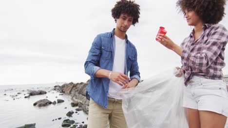 african american couple collecting garbage in a plastic bag and high fiving each other