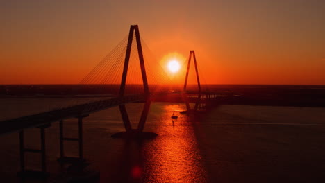 aerial drone shot of boat traveling under ravenel bridge at sunset