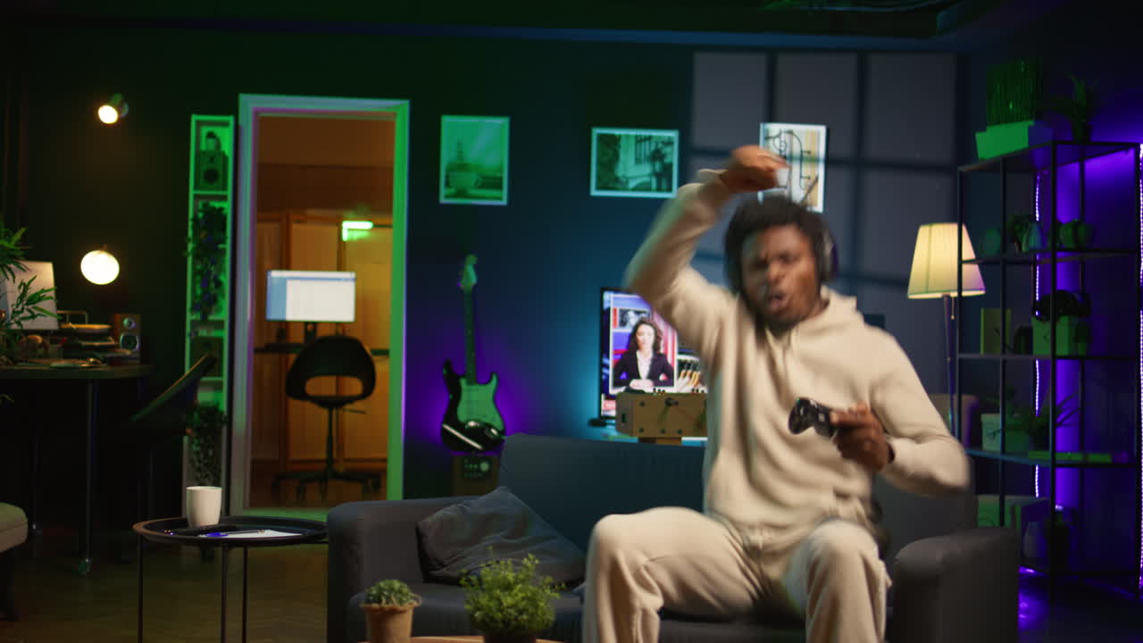 hombre alegre en su apartamento jugando videojuegos en el sofá, disfrutando de un día libre del trabajo. jugador negro luchando contra enemigos en shooter multijugador en línea en la consola de juegos. cámara b.