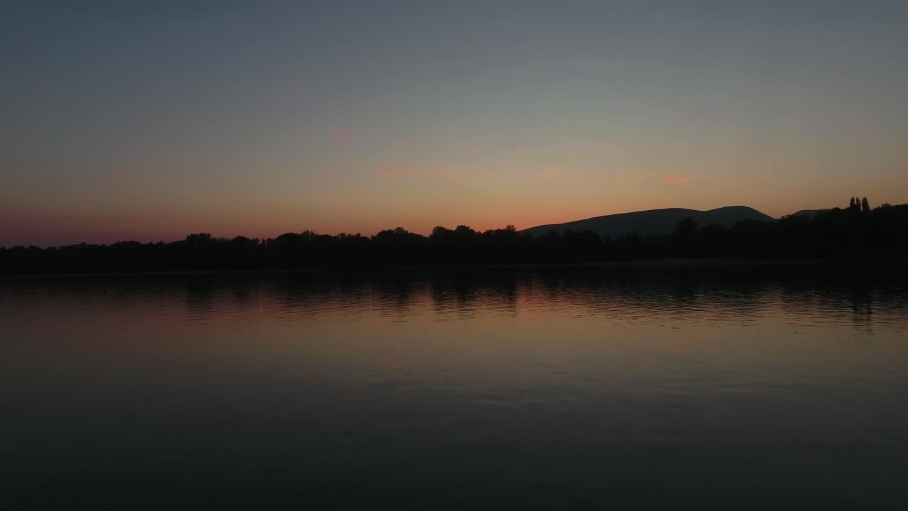 Aerial shot of a sunset or sunrise over the water, than ascending, rising up to reveal a wider scene