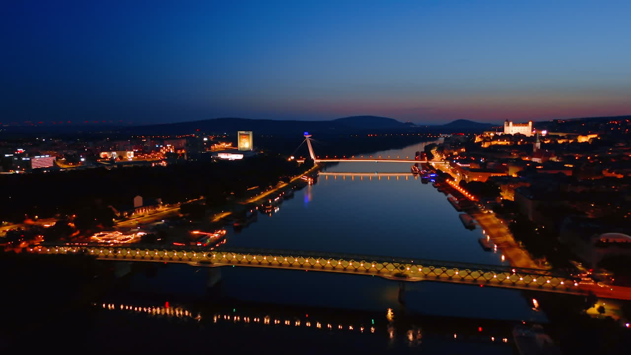 Lights are on at the Old Bridge and UFO bridge over the Danube. Night view of Bratislava, Slovakia at night. Aerial view
