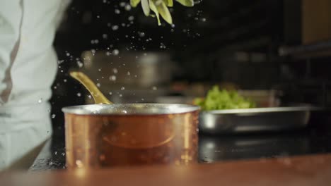 the cook shakes the greens he extracted from the water and a close-up slow motion view of the water drops