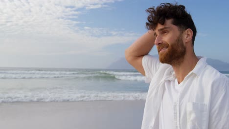 Side-view-of-young-caucasian-man-walking-and-looking-around-at-beach-on-a-sunny-day-4k