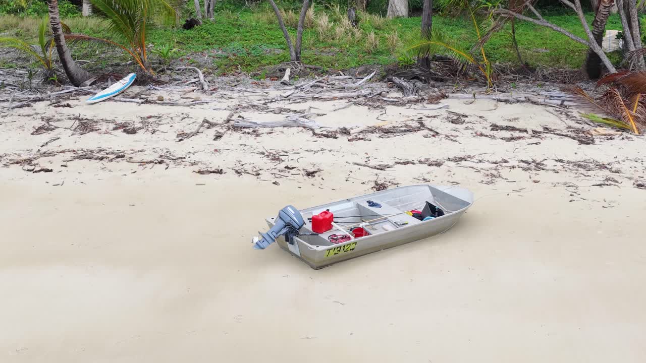 Aerial camera slowly approaches small aluminum boat on sandy beach, tropical rainforest background, daylight