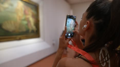 mujer tomando una foto de una pintura en un museo de arte