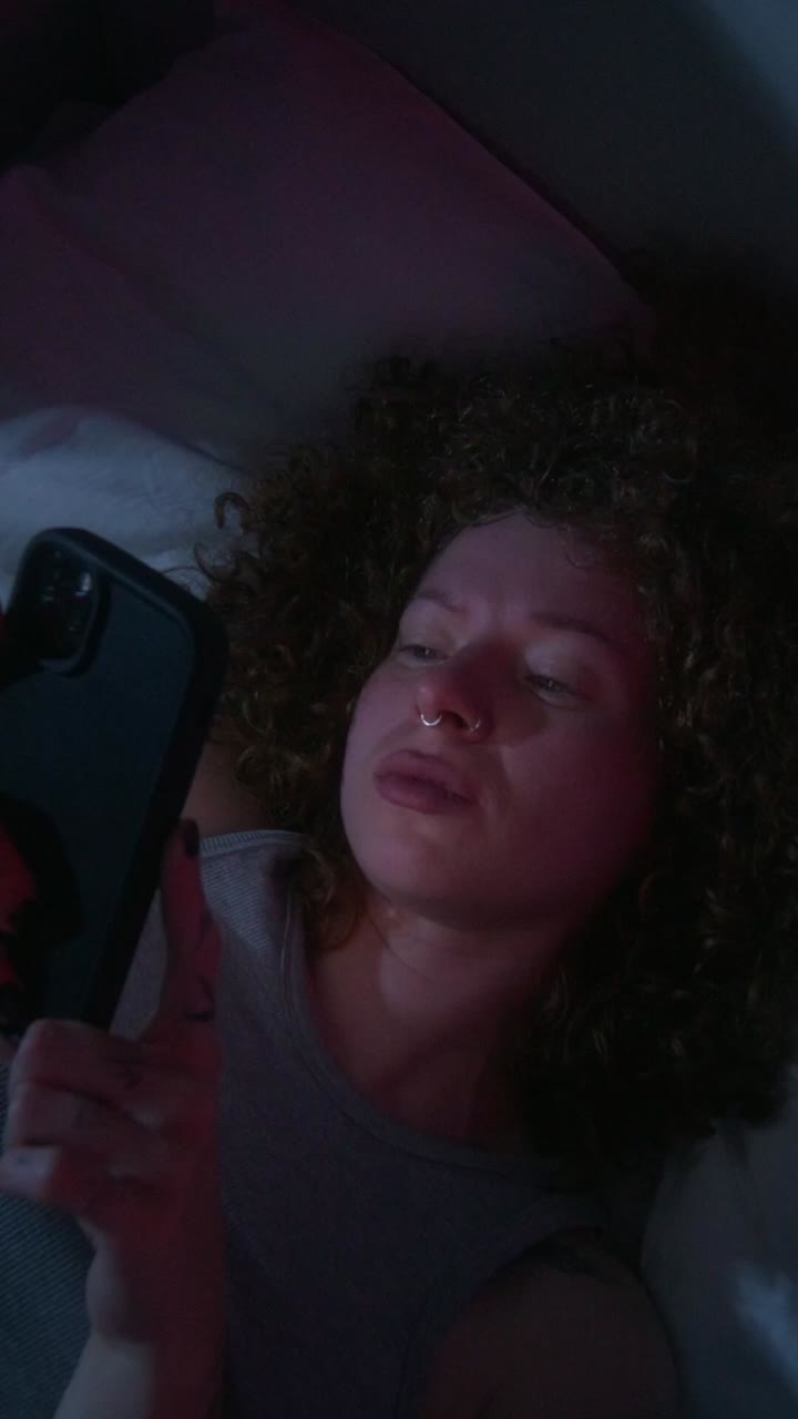 joven acostada en la cama mirando un teléfono por la noche