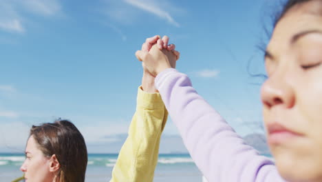 diverse female gay couple raising and holding hands at the beach