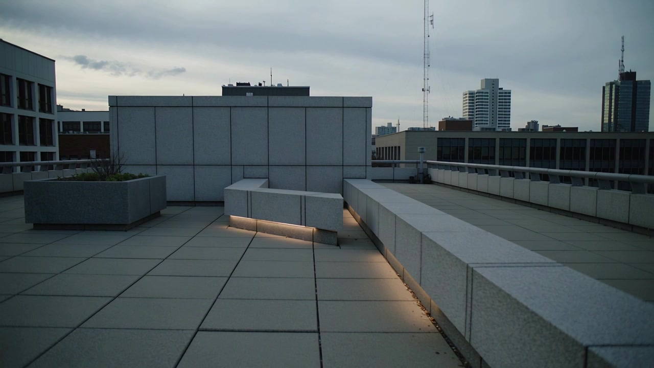 Banco de hormigón bajo y brillante que emite una cálida luz LED en una terraza en la azotea mientras las nubes se desplazan lentamente
