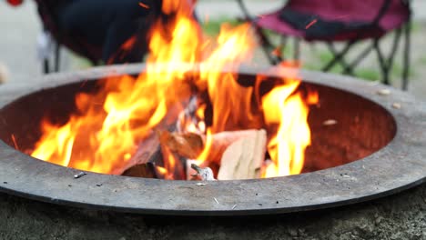 firewood being added to burning flames of campfire in fire pit, static