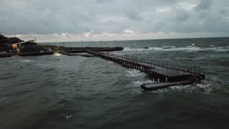 drone antena sobre océano melbourne ondulado ventoso nublado gente caminando en el muelle