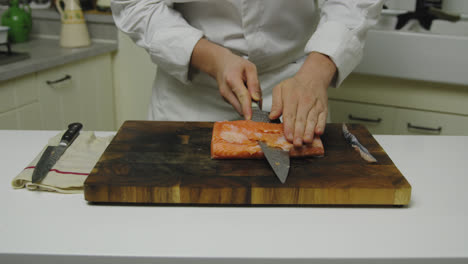 starred chef cutting fresh salmon fillet into slices on wooden board,close up