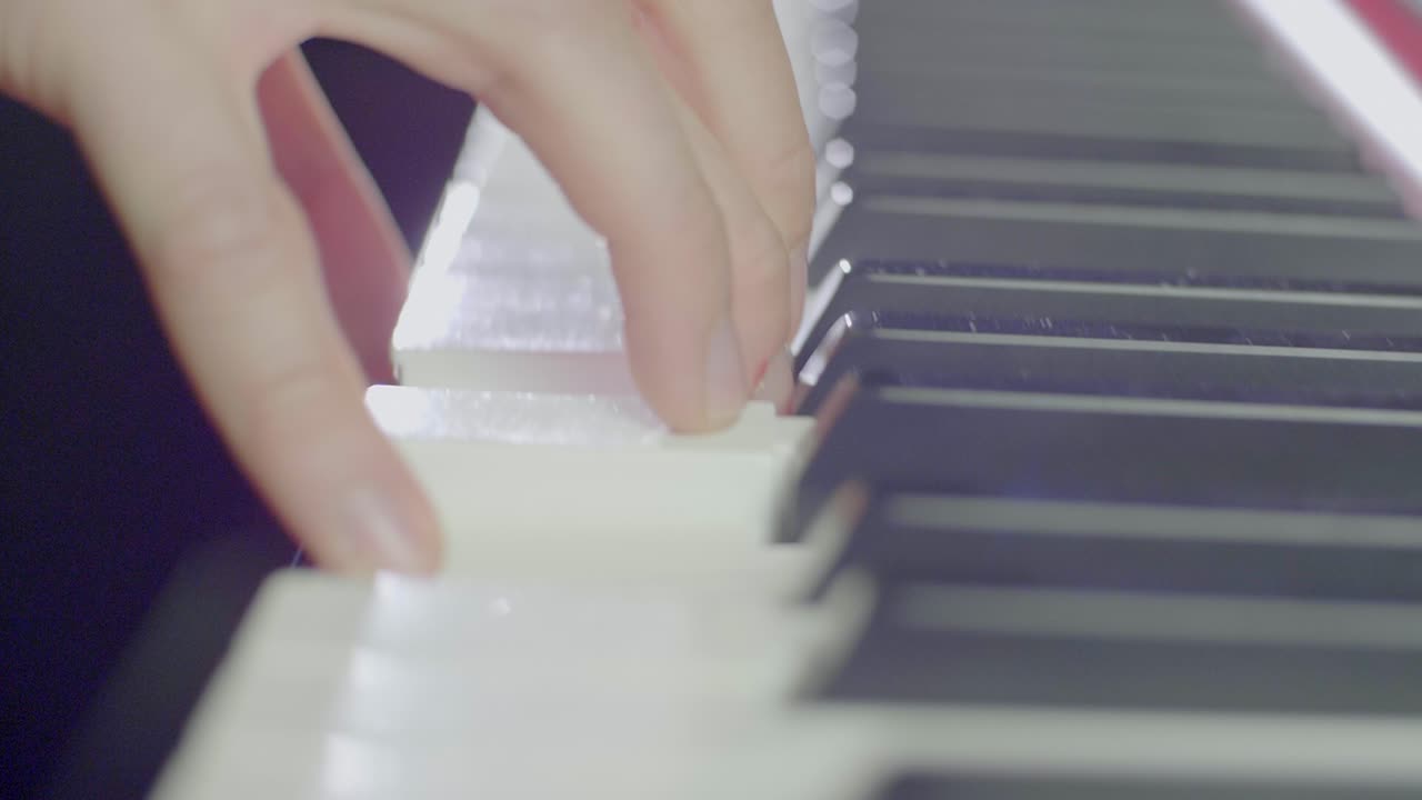 Close up of a keyboard players hand sliding up keys and landing on a chord on an electric stage piano synthesizer keyboards buttons, knobs and faders. Backwards dolly movement, stage light scenery.