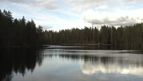 aerial, drone shot low over reflecting surface of a calm lake luukinjarvi, partly sunny, spring day, in luukki, espoo, finland