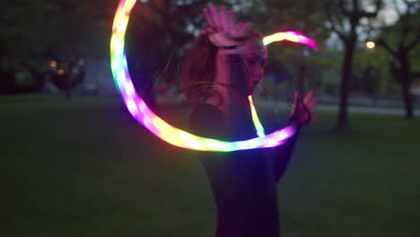 woman twirling led fans in twilight lit park, smiles