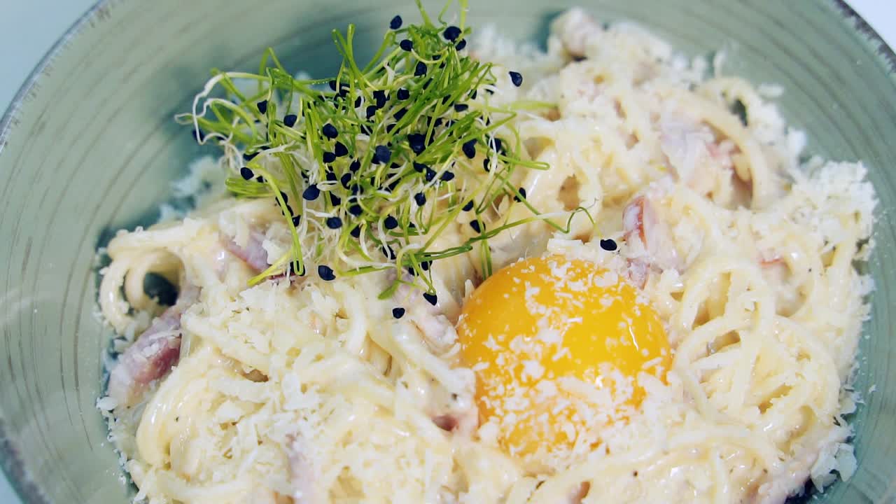 Ready-made dish decorated with green sprouts. Delicious cooked italian pasta with yolk and cheese. Chef completes cooking dish in the restaurant. Close-up