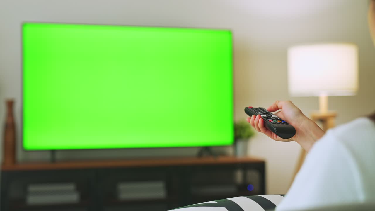 나무와 램프와 함께 거실에 tv 녹색 스크린, 소파에 앉아있는 여성, 집에서 영화를 보는, 광고를위한 크로마 키 스크린.