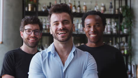 portrait of male owner of restaurant bar with team of male waiting staff standing by counter