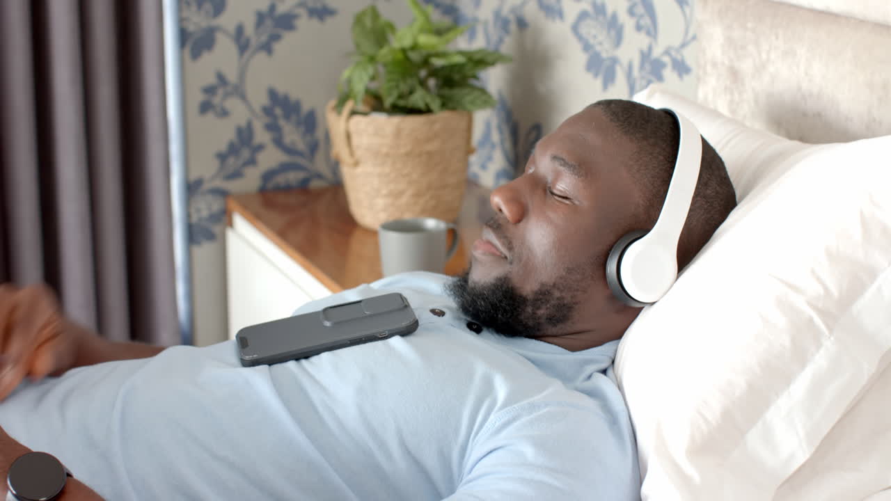 Uomo che si rilassa a casa, sdraiato sul letto con cuffie e smartphone.