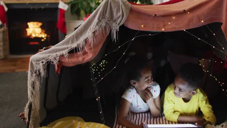 hermanos africanos americanos felices usando una tableta en una tienda de campaña improvisada