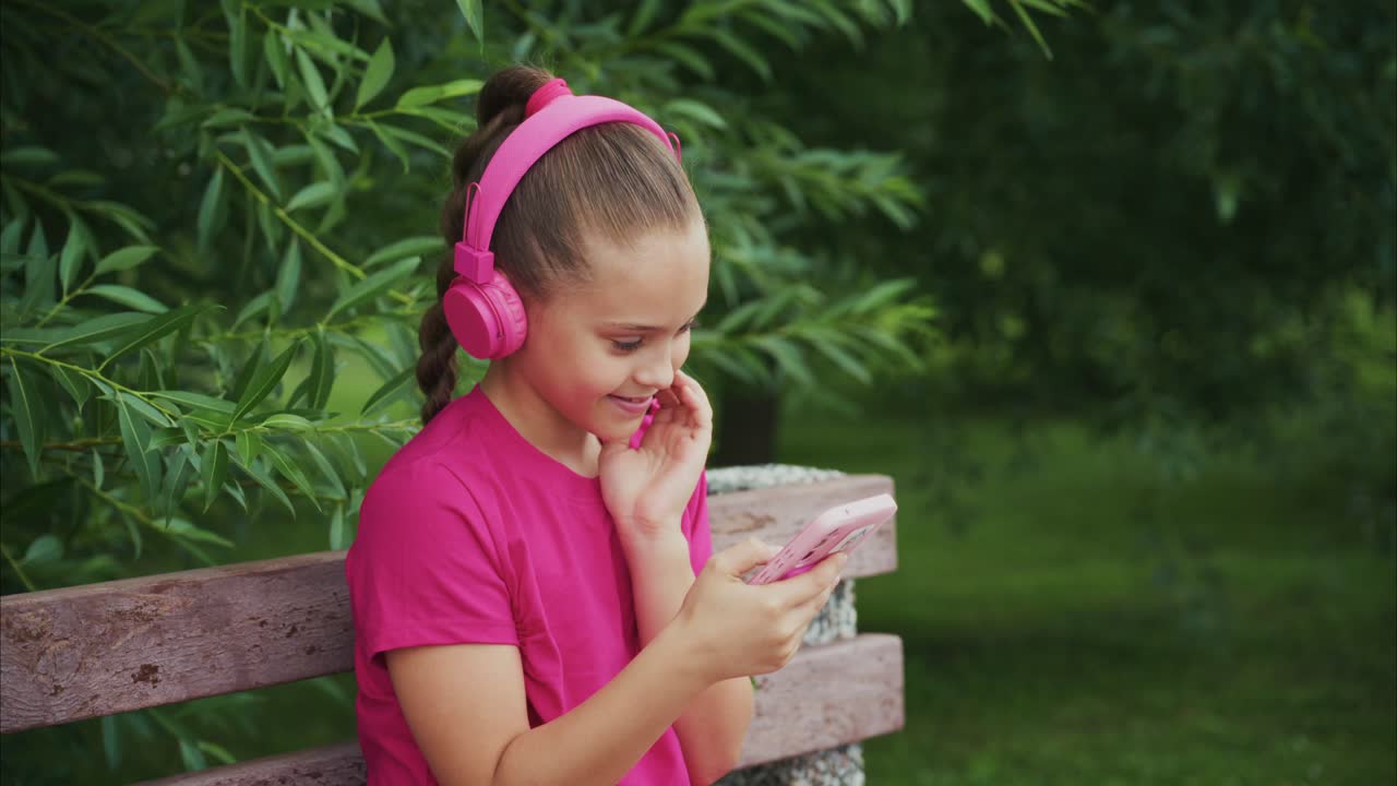 A Young Girl Enjoying a Joyful Moment While Listening to Music with Headphones, Engaged with Her Phone in a Lush Green Outdoor Setting