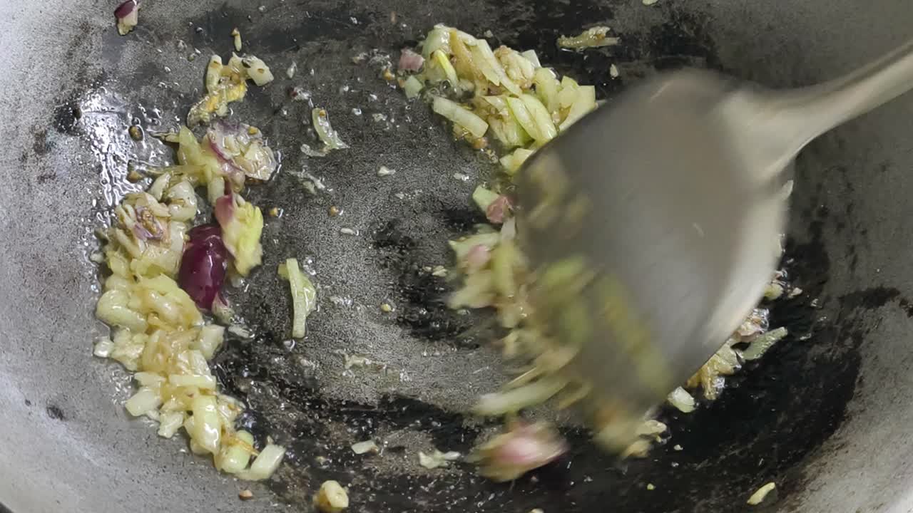 A chef is sautéing sliced onions in a hot wok using palm oil, creating a wonderful, savory aroma. The cooking process is a key step in preparing an appetizing meal
