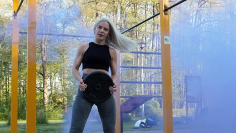 blonde girl with training weight turn to camera in slow motion blue smoke