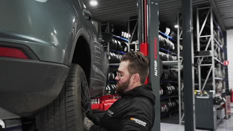 Man-rolling-tire-and-lifting-it-up-to-the-car-to-fix-the-tire,-mechanic-in-a-shop-at-work