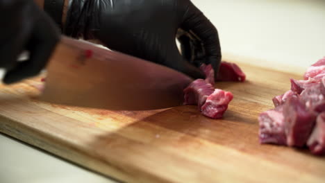 el chef está cortando en cubitos el plato de carne fresca más delicioso, usando guantes negros y un cuchillo de chef afilado