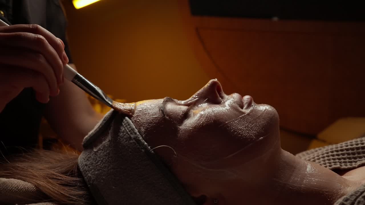 Schoonheidsspecialiste brengt gezichtsmasker aan op gezicht van vrouw in een spa