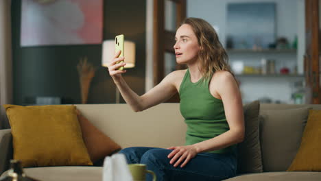 mujer sorprendida mirando teléfono inteligente sentado sofá. emocionada chica cubriendo la boca mano
