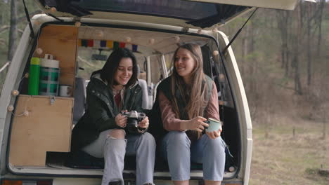 two young girl friends chat in the back of a caravan in the middle of the forest