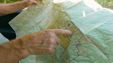 weathered hands following hiking trail on paper map