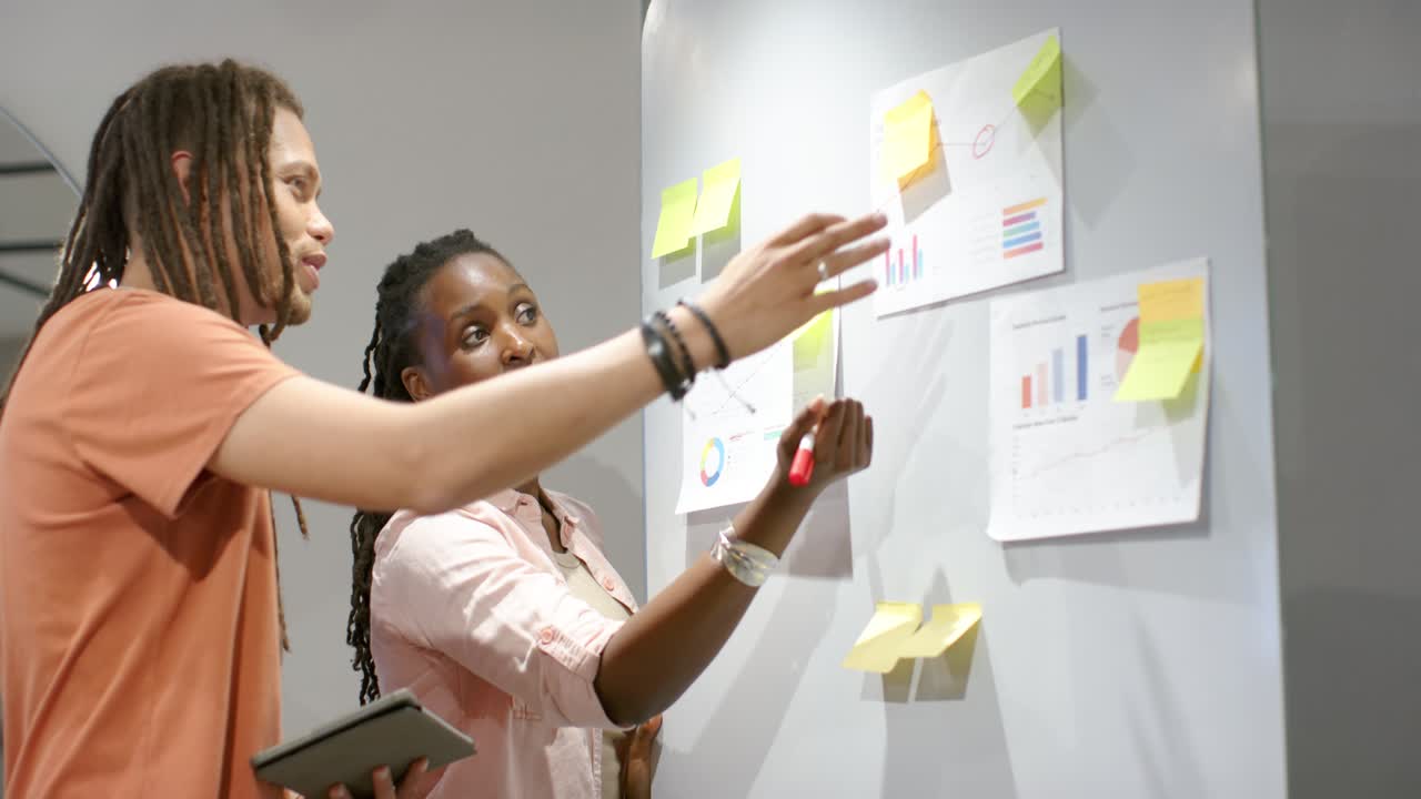 African coworkers at office board woman starting marking charts with red marker man holding tablet