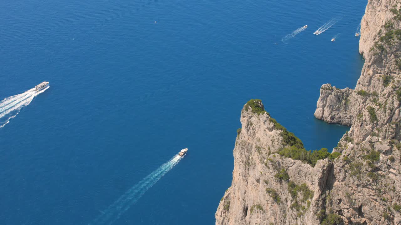 toma cinematográfica de alto ángulo sobre barcos a motor que navegan sobre las cristalinas aguas azules del mar tirreno, isla de capri, italia a lo largo de acantilados rocosos
