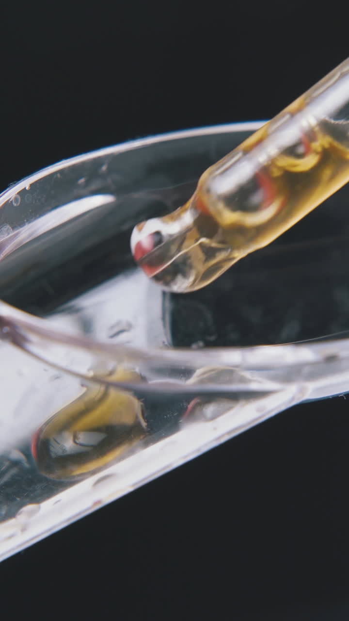 person drops light brown water into transparent measuring spoon on black background extreme close view