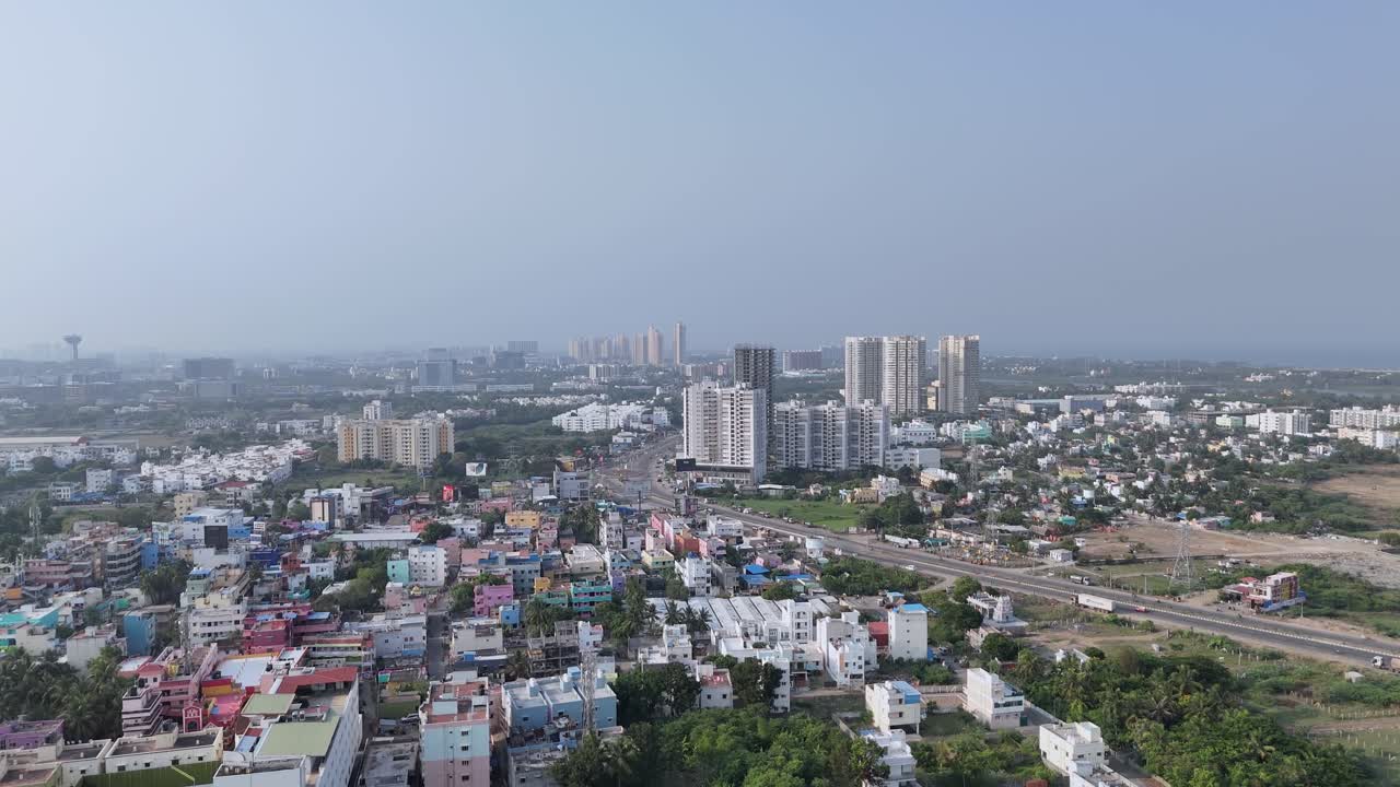 An aerial footage of Indian city hazy daytime overlooking a sprawling urban and suburban landscape. there is a mix of low-rise residential and commercial buildings with varied roof colors