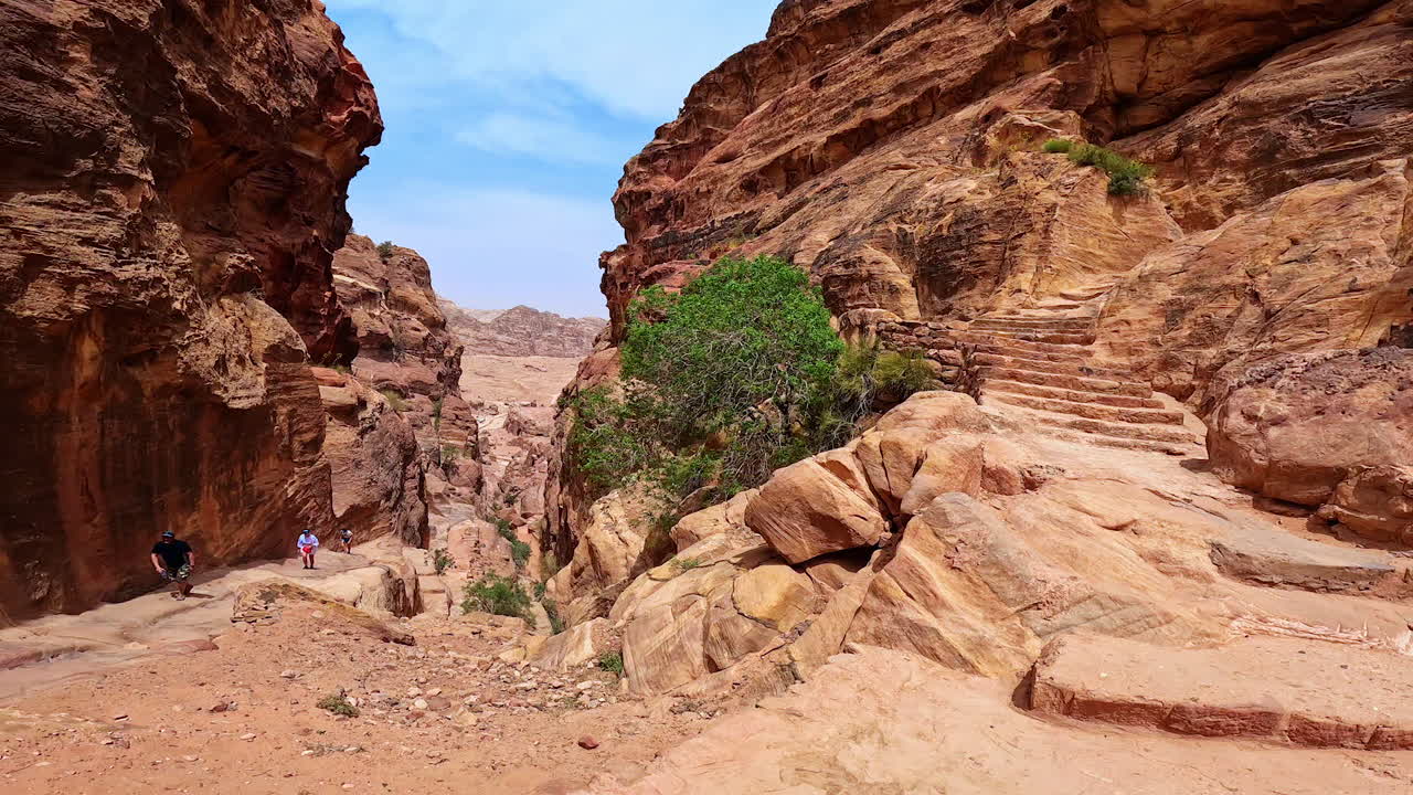 People go along the cliff rock on hot sunny day. Travelers walk to Petra, Jordan, West Asia.