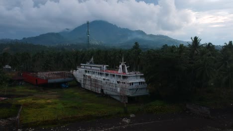 aerial drone view of an abandoned cruise shipwreck on an isolated tropical island with a dormant volcano in the foreground