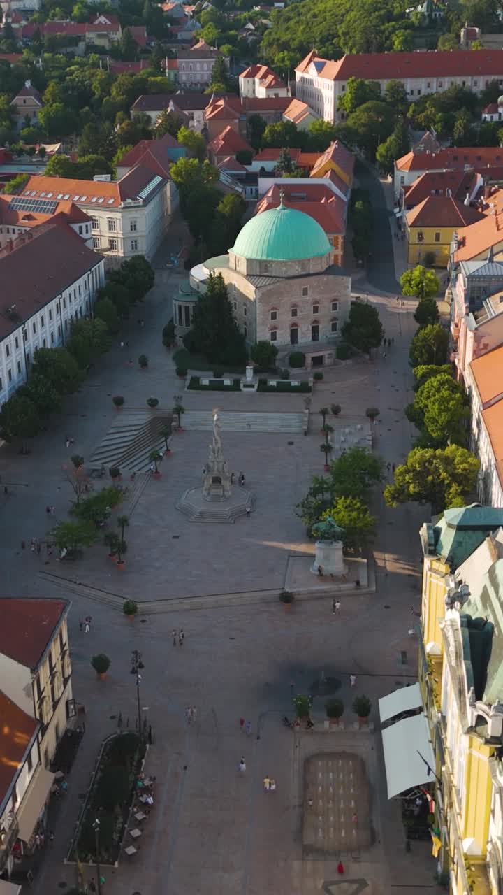 Flying down toward Széchenyi Square in Pécs, focusing on the mosque and surrounding cityscape. Vertical
