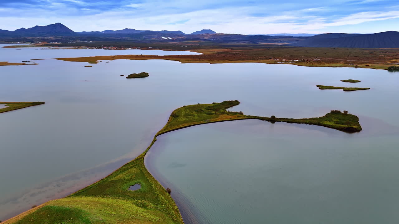 Unusual shape of little islands in the waterscape. Mountain range at horizon. Iceland shoreline. Aerial view.
