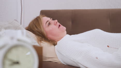 close up of woman lying on couch during coaching session listening intently to off camera coach and responding verbally, white sweater contrasts brown couch background expressive features captured
