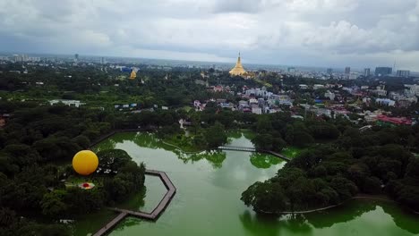 a sweeping panoramic aerial shot of yangon, myanmar, featuring the tranquil kandawgyi lake and the majestic shwedagon pagoda, providing a stunning view of the city and its cultural landmarks.