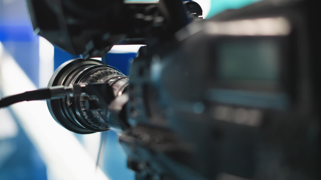 Close up camera lens and focus ring with cables reflecting blue studio lights, showcasing intricate optical elements, highlighting precision mechanism and lens coating details broadcast filmmaking